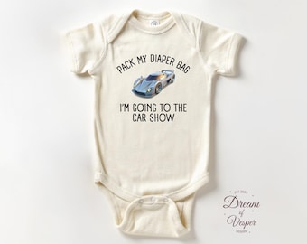 Puede incluir: Body de bebé color crema con el texto "PACK MY DIAPER BAG I'M GOING TO THE CAR SHOW" y un gráfico de coche deportivo azul. El body es de manga corta y tiene cierre de corchetes. El diseño incluye el texto "Dream of Vesper Design".
