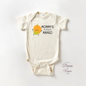 May include: Cream-colored baby onesie with the text "Mommy's Little Mango" and a cartoon mango illustration. The mango is orange and yellow with a green stem and smiling face. The onesie has short sleeves and a snap closure.