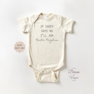 May include: Cream-colored baby onesie with the text "IF DADDY SAYS NO I'LL ASK Auntie Angelina" in black. The onesie has short sleeves and a snap closure. A small sticker says "SHIPS NEXT DAY".