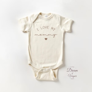 May include: Cream-colored baby onesie with short sleeves. The text "I LOVE MY mommy" is printed in brown script, with a small heart below. The Dream of Vesper Design logo is in the bottom right corner.