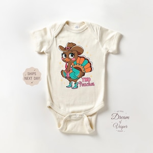 May include: Cream-colored baby bodysuit featuring a cartoon turkey wearing a cowboy hat, turquoise vest, and boots. The turkey has a colorful tail and the text "Two Peaches". A cute Thanksgiving or fall-themed outfit.