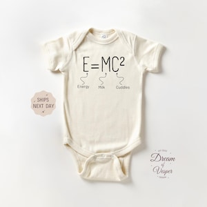 May include: Cream-colored baby onesie with the equation E=MC² printed in black. Below the equation are the words "Energy", "Milk", and "Cuddles". The onesie has short sleeves and a snap closure.