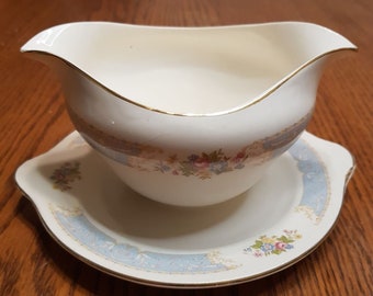 May include: A white gravy boat with a blue and gold floral pattern. The boat is on a matching saucer.