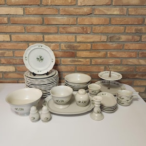May include: A complete vintage dinnerware set in cream with a green floral design. The set includes plates, bowls, cups, a serving platter, salt and pepper shakers, and a two-tiered serving tray. The plates measure approximately 10 inches in diameter.
