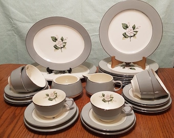 May include: A set of gray and white china dinnerware with a floral design. The set includes plates, bowls, cups, and saucers.