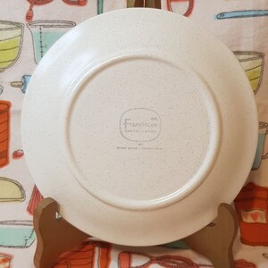 May include: White ceramic dinner plate with a speckled finish. The back of the plate has a circular logo that reads " Franciscan Co. Earthenware"