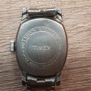 May include: Silver Timex watch with a stainless steel back and a chrome plated bezel. The watch face says "Shock Resistant" and "Timex".