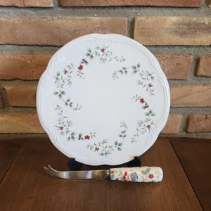 May include: White ceramic serving plate with a green and red holly pattern. The plate has a scalloped edge and comes with a matching cheese knife.