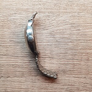 May include: A silver wristwatch with a metal band. The watch is on a wooden surface.