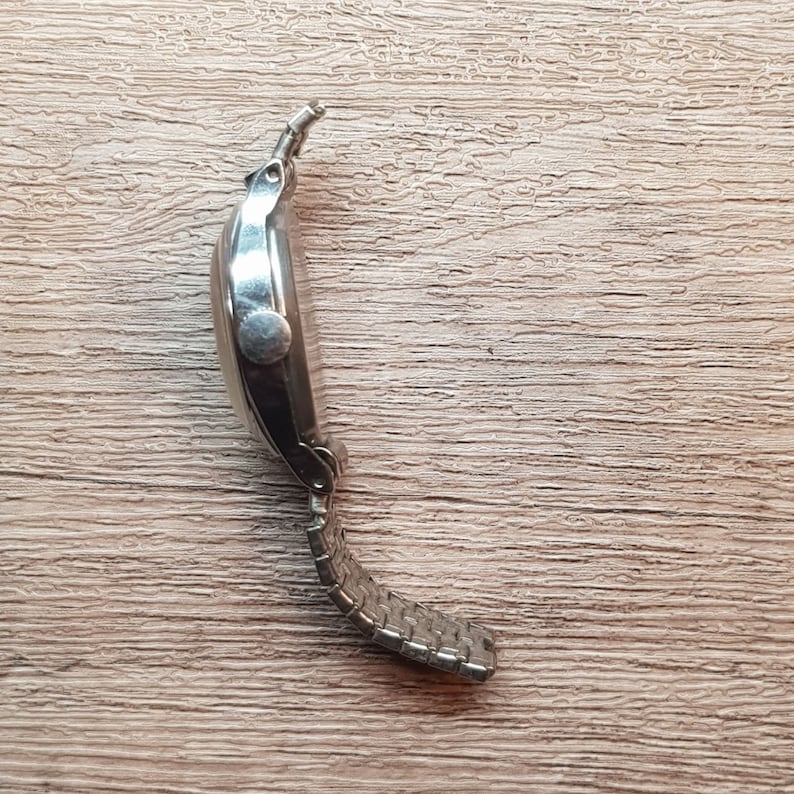 May include: A silver wristwatch with a metal band. The watch is on a wooden surface.
