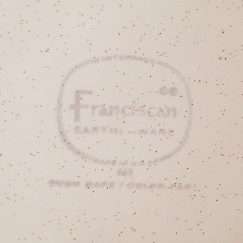 May include: Close-up of a white ceramic plate with a brown speckled glaze. The plate has a circular logo that reads "Franciscan Co. Earthenware" in a gray font.