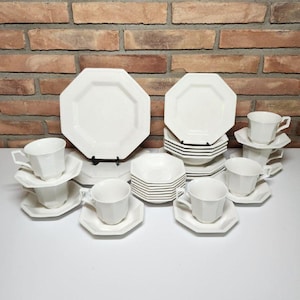 May include: A set of white octagonal dinnerware including large plates, small plates, and cups with matching saucers. The pieces feature a clean, solid white finish with distinct eight-sided edges, arranged in a collection on a flat surface.