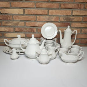 May include: A white porcelain tea set with a teapot, creamer, sugar bowl, and cups. The set also includes a serving dish and a stack of plates.
