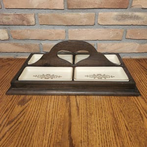 May include: A wooden serving tray with a heart-shaped cutout in the handle. The tray has five small ceramic dishes with a floral design.