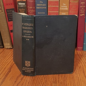 Może przedstawiać: Twarda okładka książki w ciemnoniebieskim kolorze z pozłacanymi napisami na grzbiecie. Tytuł to "P. VERGILI MARONIS OPERA", a autorem jest "A. SIDGWICK". Książka została wydana przez Cambridge University Press.