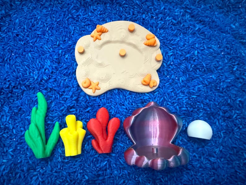 colorful ocean-themed toys, including a beige island with starfish and orange accents, green and yellow seaweed, red coral, a purple and blue shell, and a white pearl that piece together.