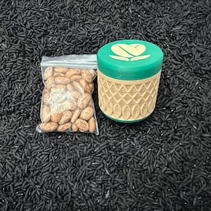 May include: A clear plastic bag filled with pinto beans next to a green and tan container with a coffee bean design on the lid. The objects are on a bed of black rice.