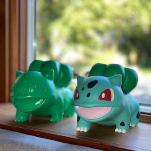 May include: Two green and blue Pokemon figures, one is a Bulbasaur and the other is an Ivysaur. The figures are made of plastic and have a cartoon style.
