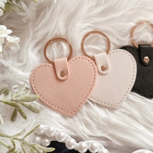 May include: Three heart-shaped keyrings with gold rings. The keyrings are pink, white and black.