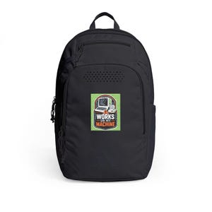 Peut inclure: Un sac à dos noir doté d'un écusson rectangulaire sur fond vert. L'écusson présente une illustration d'ordinateur vintage et le texte "WORKS ON MY MACHINE" en lettres blanches et orange, avec une petite icône de triangle d'avertissement.