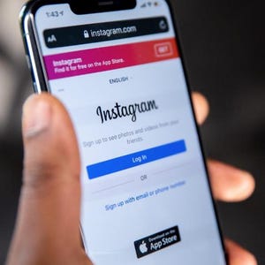 May include: A smartphone displaying the Instagram app interface. The screen shows the Instagram logo, a login button, and the option to sign up. The app store download icon is visible at the bottom.