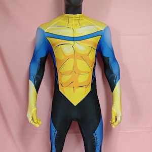 Puede incluir: Un disfraz de cuerpo entero en amarillo y azul. El disfraz presenta un pecho y hombros amarillos, con detalles azules en los brazos y las piernas. El diseño incluye un patrón estilizado de músculos abdominales.