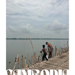May include: Two people stand on a wooden walkway over a body of water. The walkway is made of bamboo and is supported by wooden poles. The water is calm and the sky is cloudy. The text "CAMBODIA" and "KRONG KAMPONG CHAM" is visible in the image.