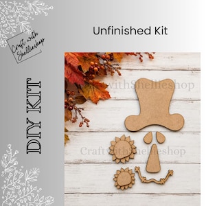 May include: An unfinished wooden DIY kit featuring a top hat shape, two small teardrop shapes, two sunflower shapes, a triangular nose shape, and a curved mouth shape, arranged on a white wood surface with autumn leaves in the corner.