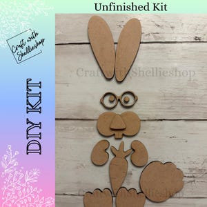 May include: A DIY kit with unfinished wooden pieces to create a bunny. The kit includes bunny ears, glasses, a nose, a carrot, feet, and a cloud-shaped piece. The text "Unfinished Kit" is at the top. The text "DIY KIT" is on the left side.