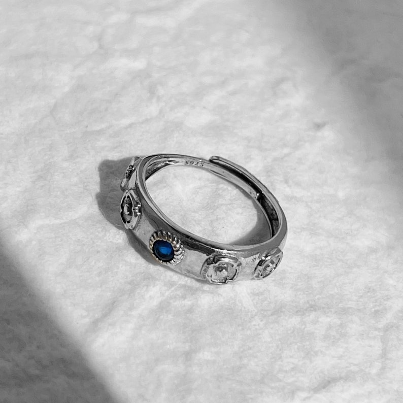 May include: Silver ring with a blue stone and decorative details. The ring has a delicate design and a subtle shine.