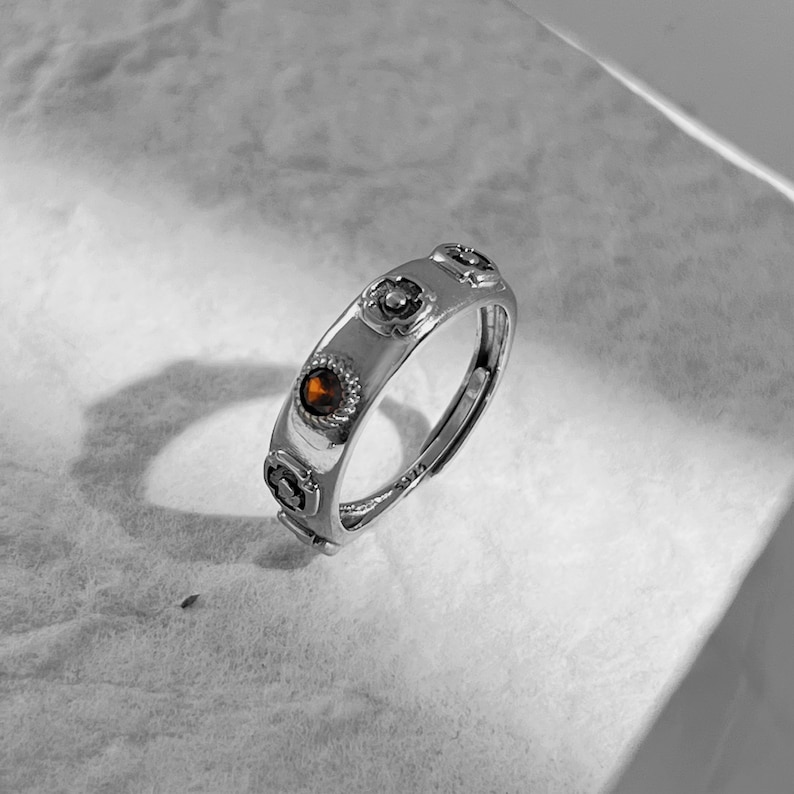 May include: A silver ring with a brown stone and four decorative accents. The ring is on a white surface.