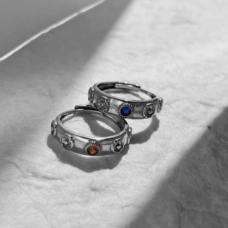 May include: Two silver rings with floral designs and small blue and orange gemstones.