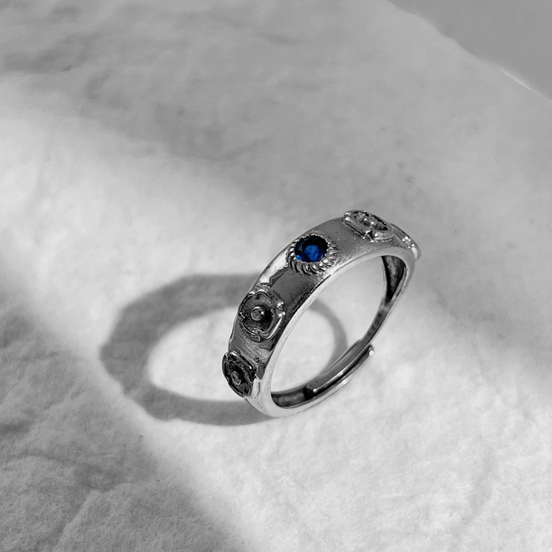 May include: A silver ring with a blue gemstone and decorative floral accents.