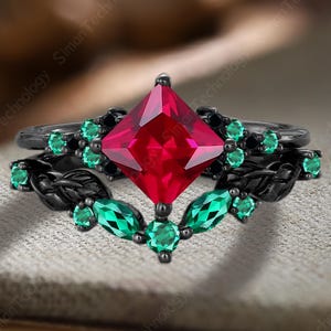 Peut inclure: Un ensemble de bagues de fiançailles noires avec une grosse pierre rouge carrée au centre. La bague est ornée de petites pierres vertes et de détails noirs en forme de feuilles. Le texte "Siman Technology" est visible.
