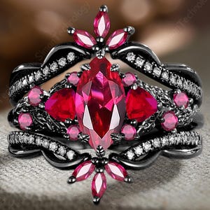 May include: A black engagement ring set with a large, marquise-cut ruby center stone and smaller ruby accents. The ring features a floral design with a halo of small diamonds. The band is black and has a textured appearance.