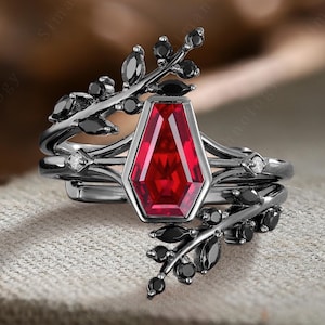 May include: A black ring with a red gemstone and black leaves. The ring is set on a brown fabric background.