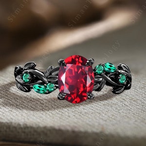 May include: Black ring with a large red oval gemstone and smaller green gemstones set in a leaf design.
