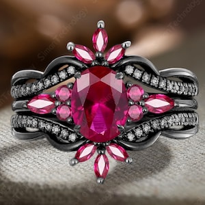 以下が含まれることがあります： 大きな楕円形のルビーのセンター石、小さなピンク色の宝石と白いアクセントストーンに囲まれた、3ピースのリングセット。リングは濃い灰色の金属バンドです。セットはニュートラルカラーの表面に表示されます。