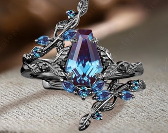 Puede incluir: Un juego de anillos negro con una gran piedra preciosa azul rodeada de piedras azules más pequeñas. El anillo presenta un delicado diseño de hojas.
