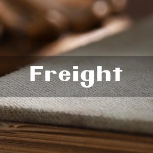 Puede incluir: Primer plano de una tela texturizada de color gris claro con la palabra "Freight" en letras blancas. La tela parece ser parte de un objeto más grande, posiblemente un libro o un mueble. El fondo está borroso.
