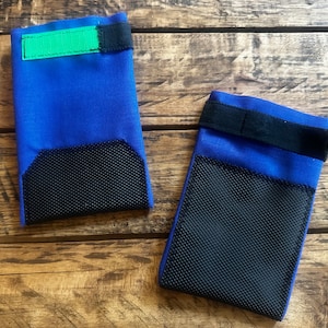 May include: Two blue fabric dog booties with black mesh pads on the bottom. One bootie has a green strap and the other has a black strap.