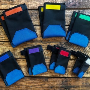 May include: Eight black fabric dog booties with different colored accents. The booties have blue fabric on the bottom and a velcro strap on the top. The accents are orange, yellow, green, purple, red, and white.