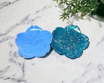May include: Two small flower-shaped resin dishes. One is light blue with a swirl design, the other is teal with iridescent glitter.