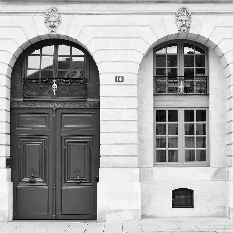 May include: Black and white photograph of a building facade featuring a dark wooden door and arched windows. The building has a stone exterior with decorative carvings above the windows. The number 14 is visible on the wall.
