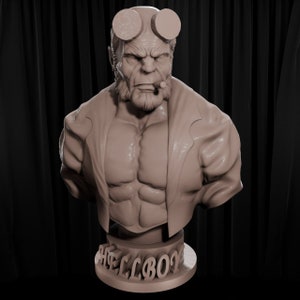 Puede incluir: Un busto esculpido detallado de Hellboy, un superhéroe ficticio, con un cigarro en la boca y una expresión seria. La escultura está hecha de un material marrón claro y está montada sobre una base circular con la palabra "HELLBOY" inscrita en ella.