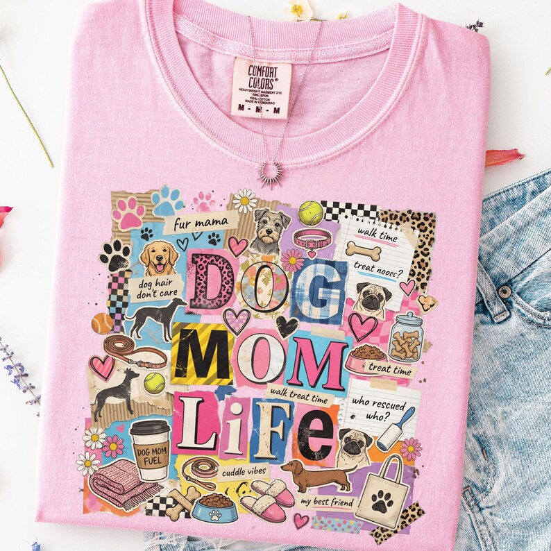 May include: A light pink t-shirt with a colorful graphic that reads "DOG MOM LIFE." The design includes dog illustrations, paw prints, hearts, and the phrases "fur mama," "dog hair don't care," and "my best friend."