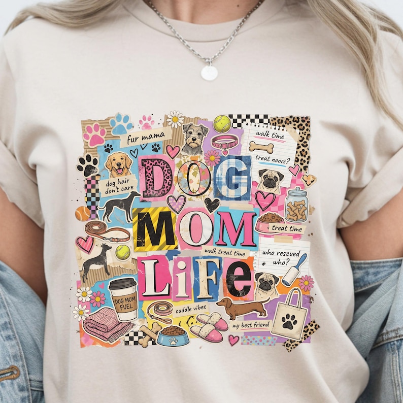 May include: Beige t-shirt with a colorful graphic design featuring the words "DOG MOM LIFE" and various dog-related illustrations. The design includes paw prints, hearts, dog breeds, and the text "fur mama".