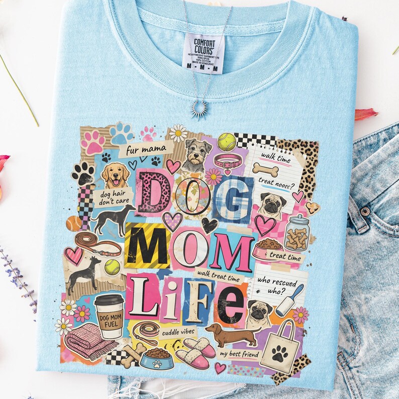 May include: Light blue Comfort Colors t-shirt with a colorful collage design. The design includes the words "DOG MOM LIFE" with dog-related graphics and phrases like "dog hair don't care" and "walk time". A silver necklace is visible.