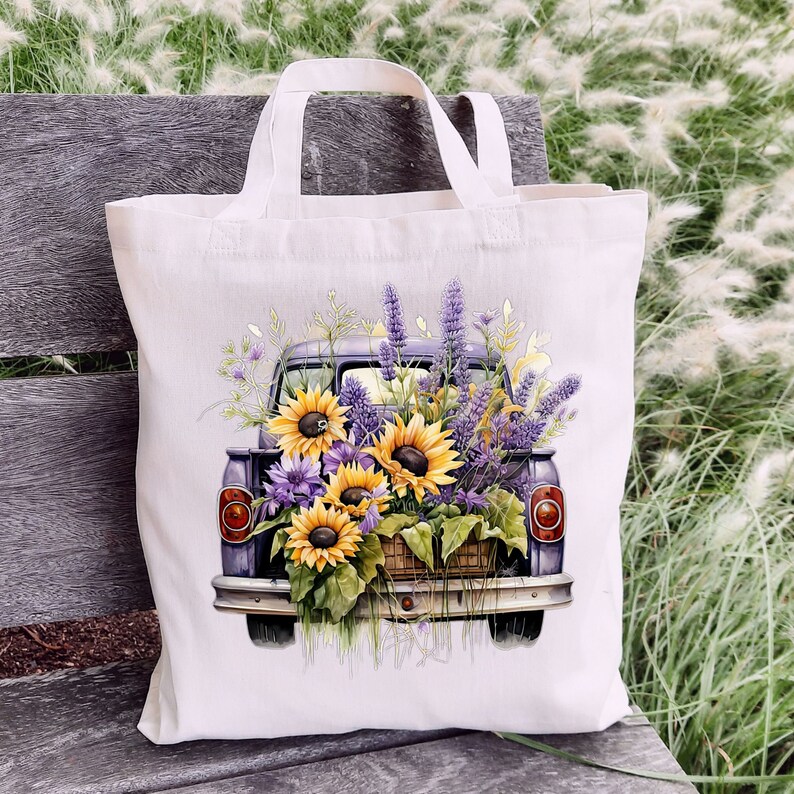 May include: A white tote bag with a purple pickup truck filled with sunflowers and lavender flowers. The truck is on a white background.