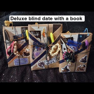 May include: Three books wrapped in brown paper, labeled Deluxe blind date with a book. Each package is tied with string and decorated with stickers, a scrunchie, a pen, and a small charm. The stickers feature various illustrations and text.